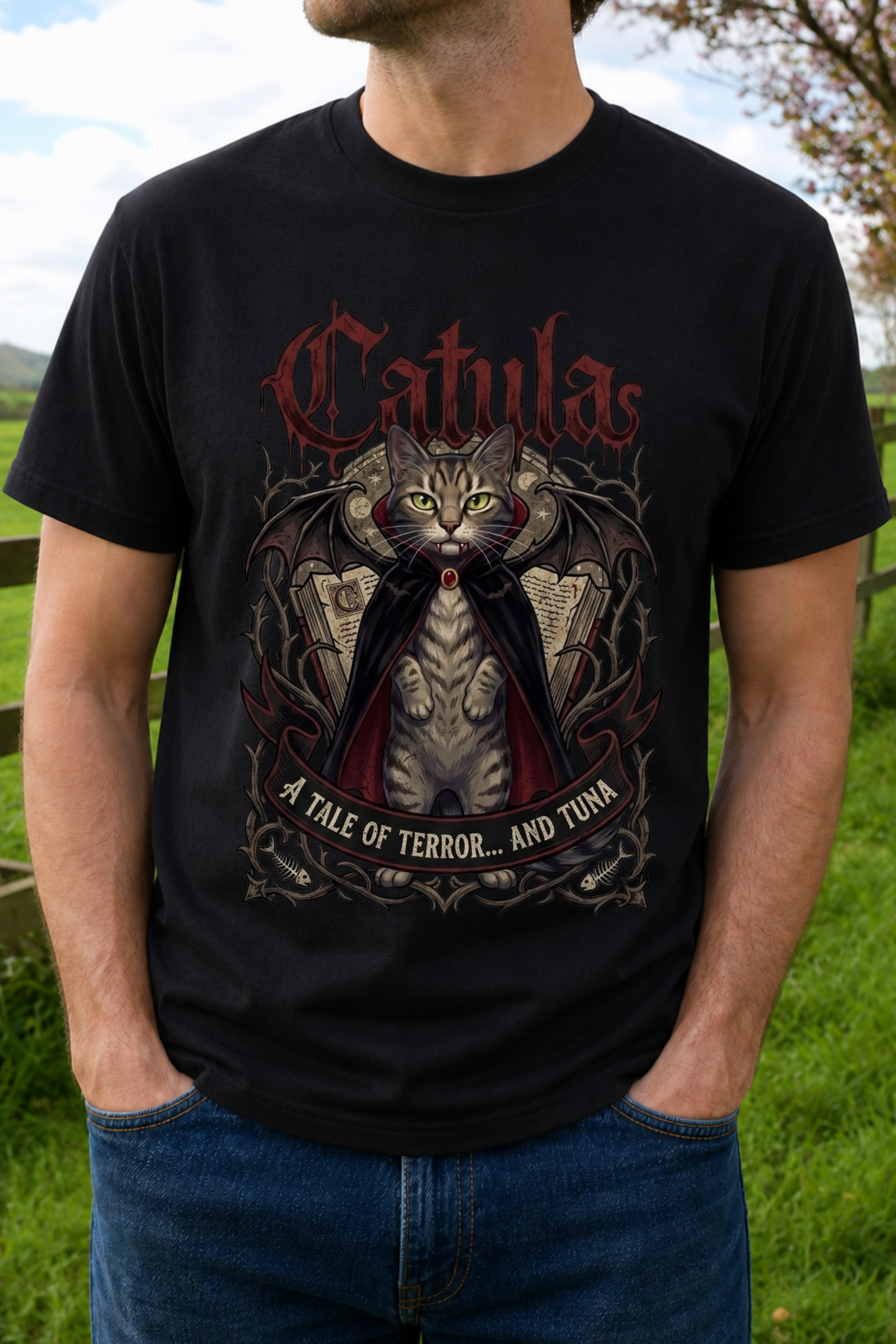 A man wearing a black graphic t-shirt with a detailed design of a cat in a cape and the word 'Catula' in gothic red lettering.