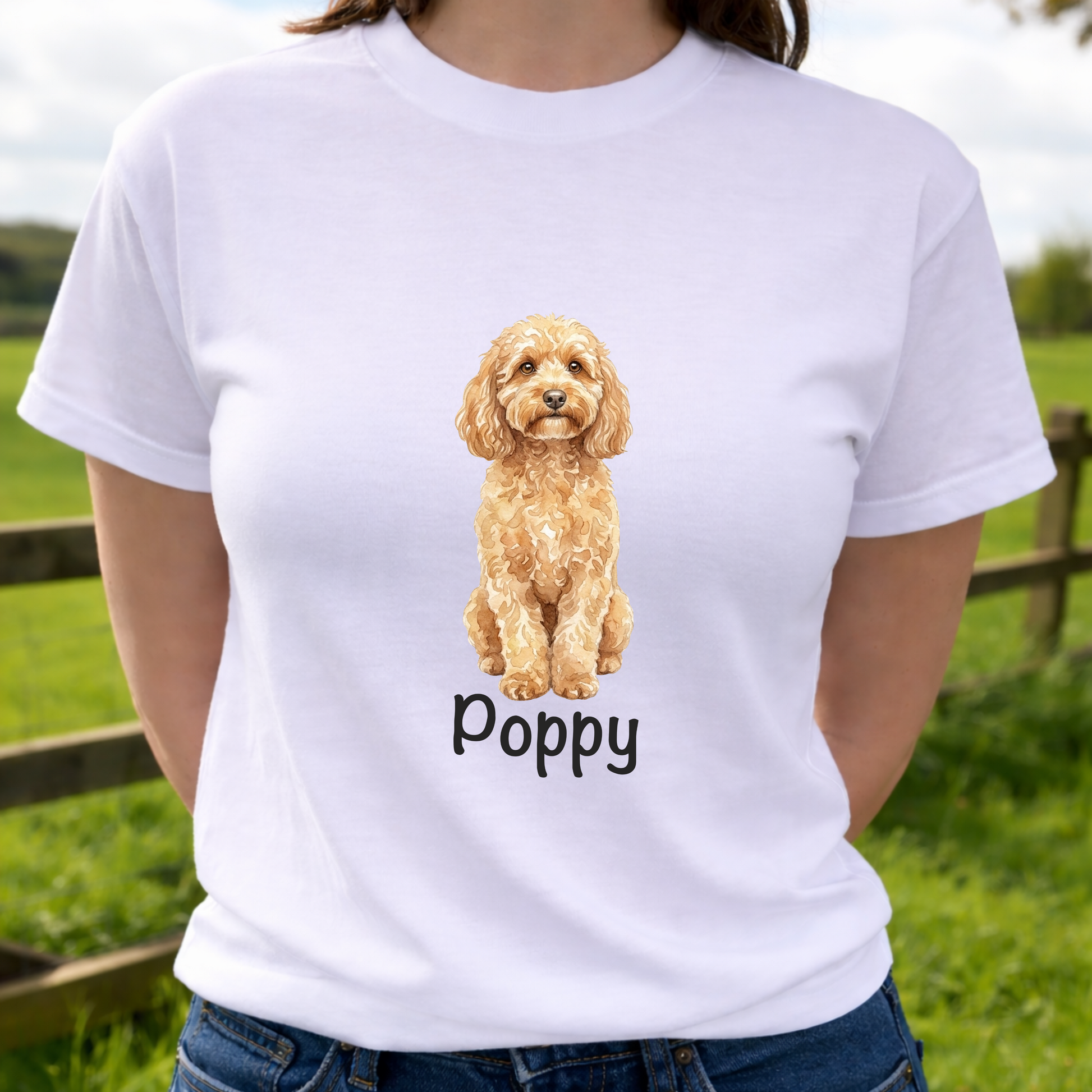 Person wearing a personalised dog white t-shirt with a watercolour cockapoo illustration and 'Poppy' text, standing outdoors.