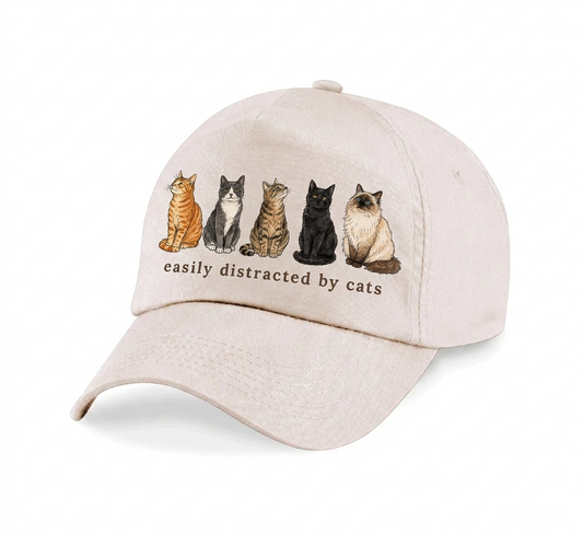 A light beige baseball cap featuring a graphic of five different cats sitting in a row above the text 'easily distracted by cats'.