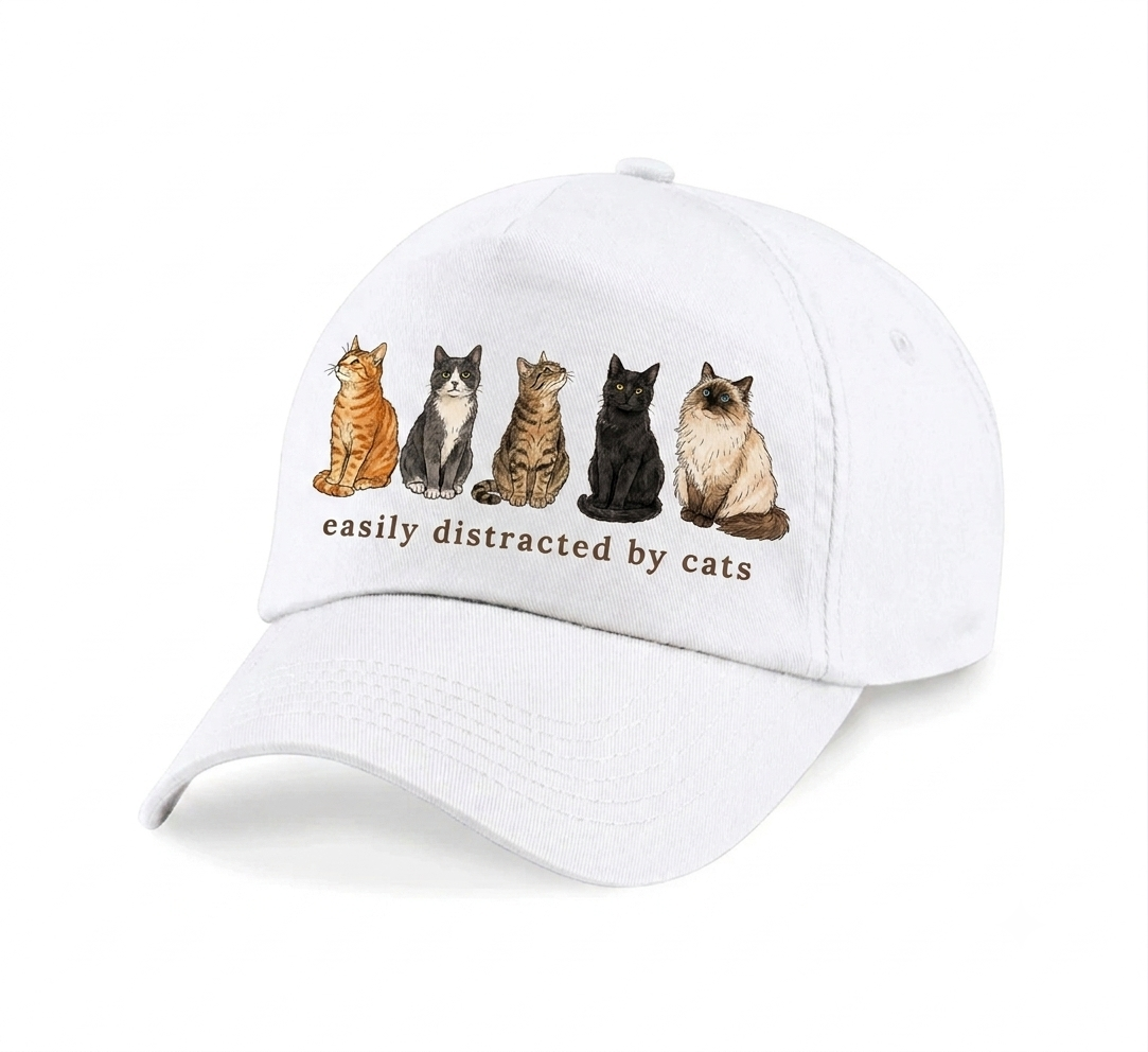 A white baseball cap featuring an illustration of five different cats sitting in a row, with the text 'easily distracted by cats' printed underneath in brown. The cap is photographed on a clean white background with a soft shadow.