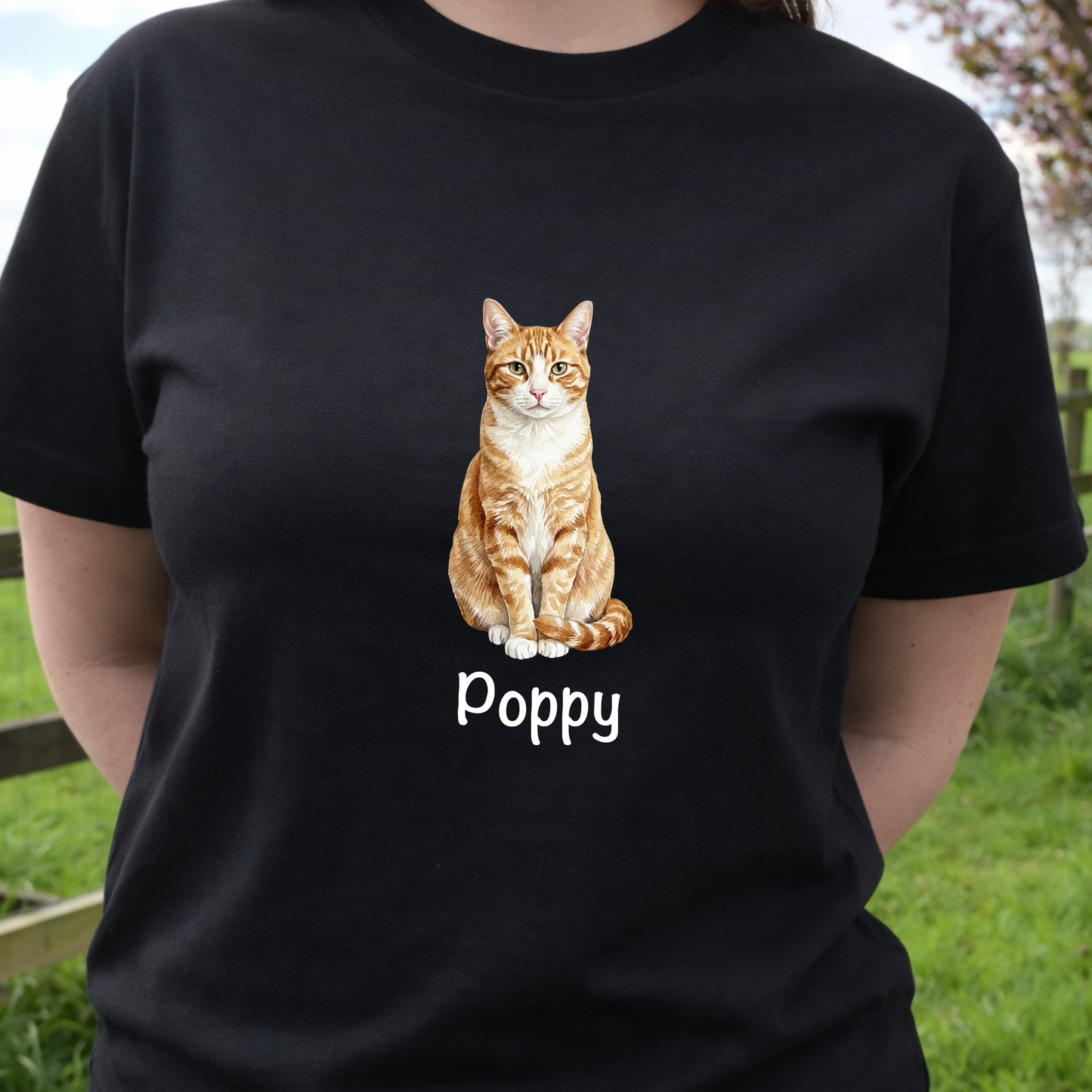Person wearing a black t-shirt with a cat illustration and 'Poppy' text, standing outdoors.