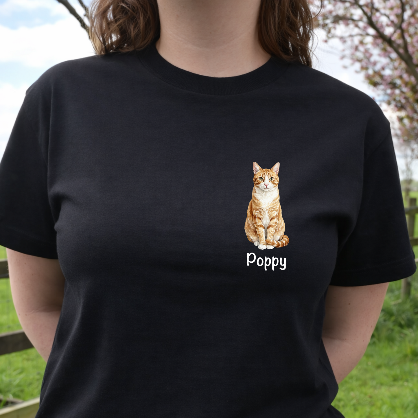 Person wearing a black t-shirt with a cat illustration and 'Poppy' text, standing outdoors.