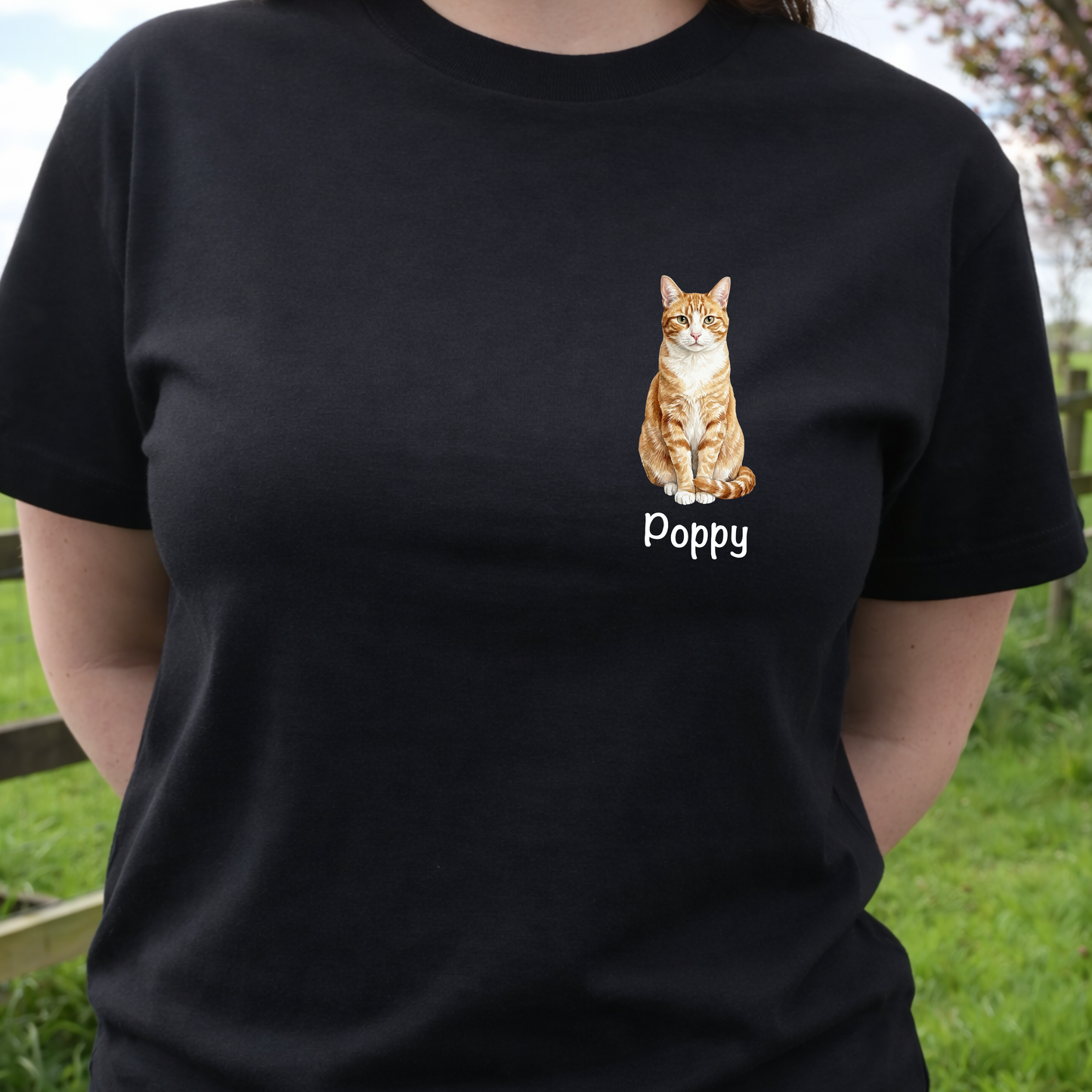 Person wearing a black t-shirt with a cat illustration and 'Poppy' text, standing outdoors.