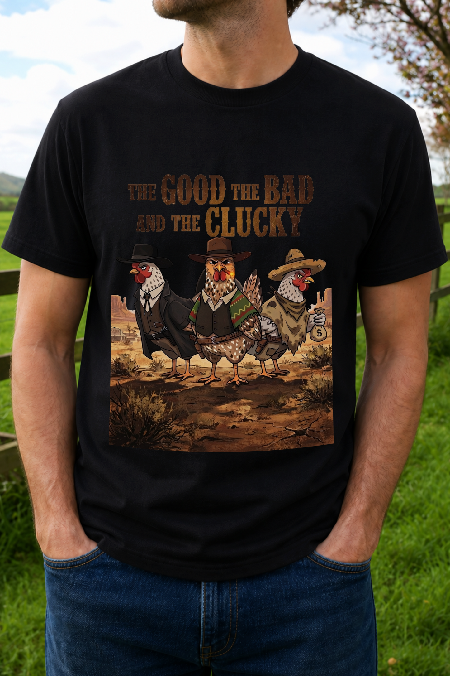 A man wearing a black graphic t-shirt with a humorous hen-themed western print that reads 'THE GOOD THE BAD AND THE CLUCKY'. The graphic features three chickens dressed in cowboy attire.