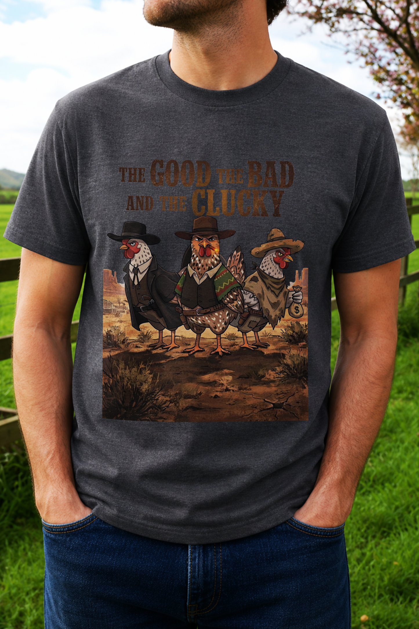 A man wearing a dark gray t-shirt with a graphic print of three chickens dressed in cowboy hats and suits, standing in a desert landscape. The text above reads 'THE GOOD THE BAD AND THE CLUCKY'.